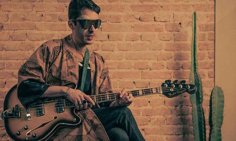 Frederico Heliodoro, usando culos escuros, est sentado e segura guitarra