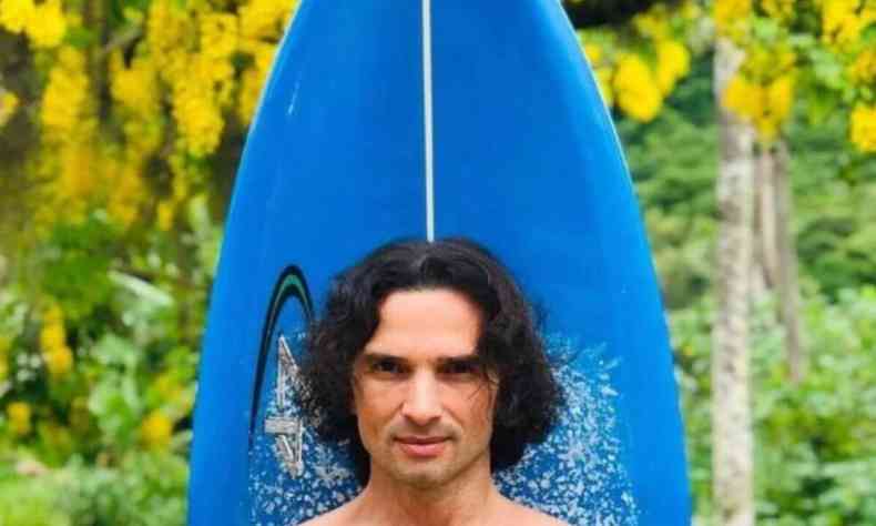 Ator Jeff Machado aparece em foto frontal, em meio a natureza. Atrs dele, h uma prancha de surf. 