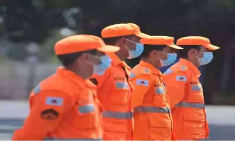 Bombeiros de uniforme laranja e enfileirados 