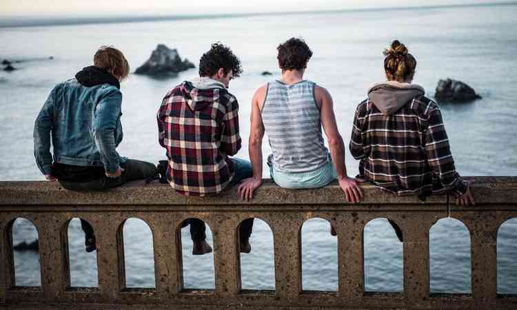 quatro homens sentados em um viaduto, de frente para o mar 