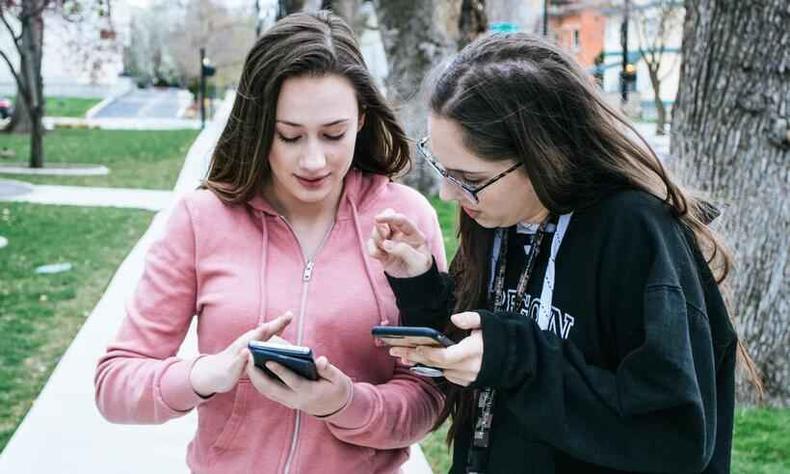Duas meninas brancas esto olhando para seus celulares enquanto andam