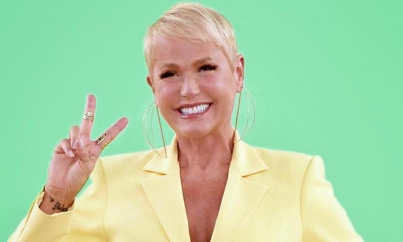 xuxa sorrindo para a foto fazendo o v com os dedos da m�o direita