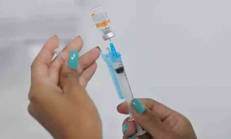 Seringa e vacina de COVID-19 sendo segurada por uma profissional da sude