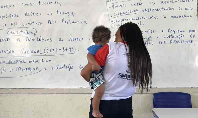 aluna segura o filho no colo em frente a quadro na escola edlzio vieira, em sergipe