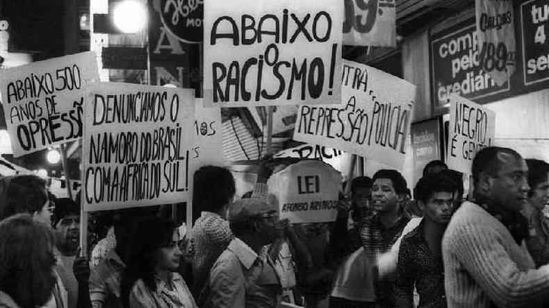 Manifestantes com cartazes onde se l: 'Abaixo o racismo', 'Denunciamos o namoro do Brasil com a frica do Sul', 'Abaixo 500 anos de opresso', 'Contra a represso policial', 'Lei Afonso Arinos' e 'Negro  gente'