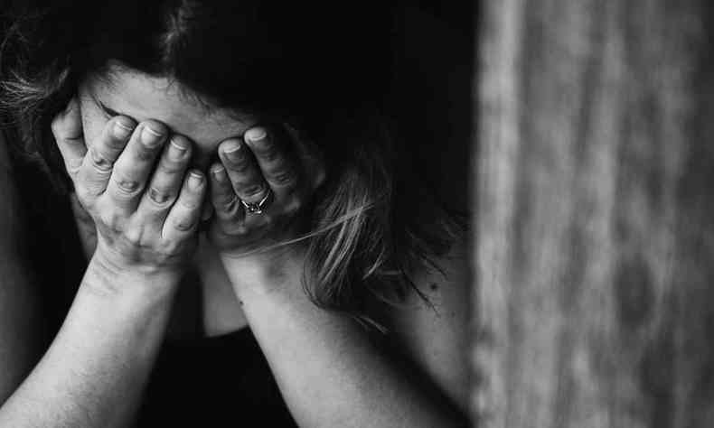 Foto em preto e branco de uma mulher chorando, escondendo o rosto nas mãos