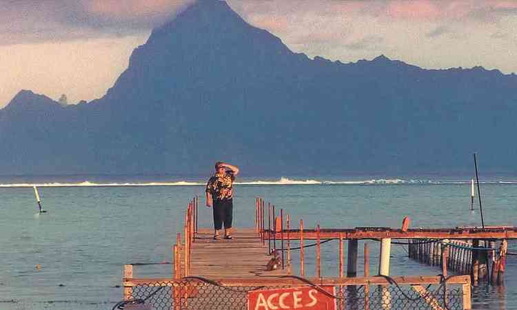 Bela paisagem do Oceano Pacfico, com homem tampando o rosto dos ltimos raios de sol, e montanha ao fundo, no filme Pacifiction