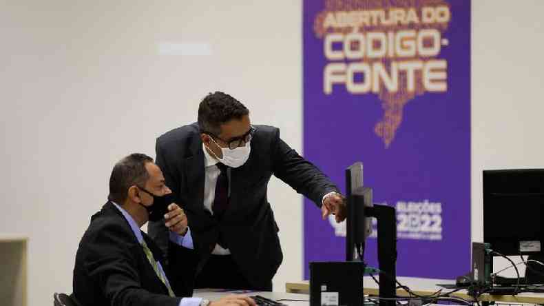 Dois homens olhando para computador, com painel atrs escrito 'Abertura do cdigo-fonte'