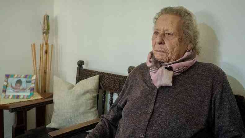 Therezinha Eugnia Pinheiro Lima, uma senhora idosa, sentada num sof com roupas de inverno