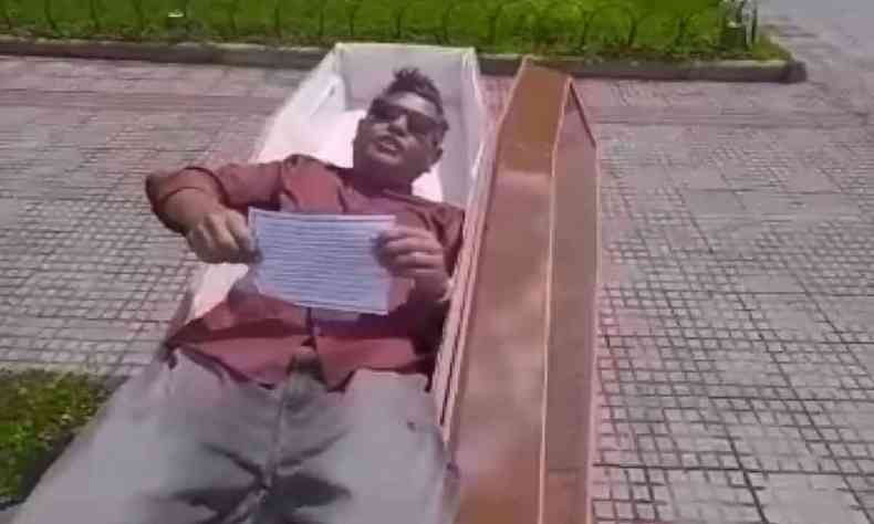 Homem deitado em caixo localizado em frente a hospital 