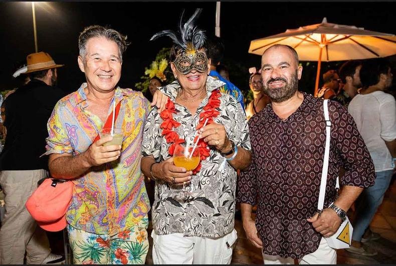 Lado a lado, Victor Dzenk, segurando um copo, Franklin Beth�nico, usando m�scara e colar de flores, e Alexandre de Castro sorriem, durante evento de carnaval no Rio de Janeiro 