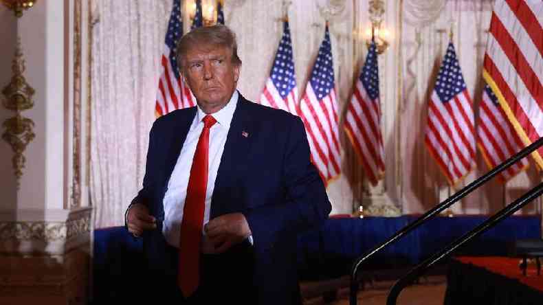 Donald Trump com olhar srio em sala repleta de bandeiras americanas