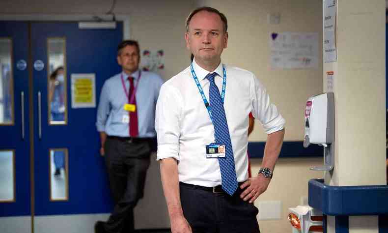 Na foto, Simon Stevens, coordenador do serviço de saúde pública inglês, posa de crachá no corredor de uma unidade de saúde