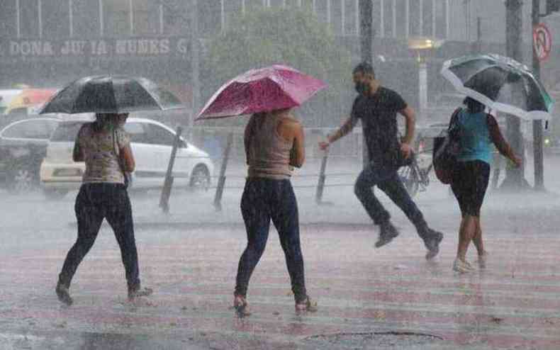 Pessoas atravessam a rua na chuva em BH