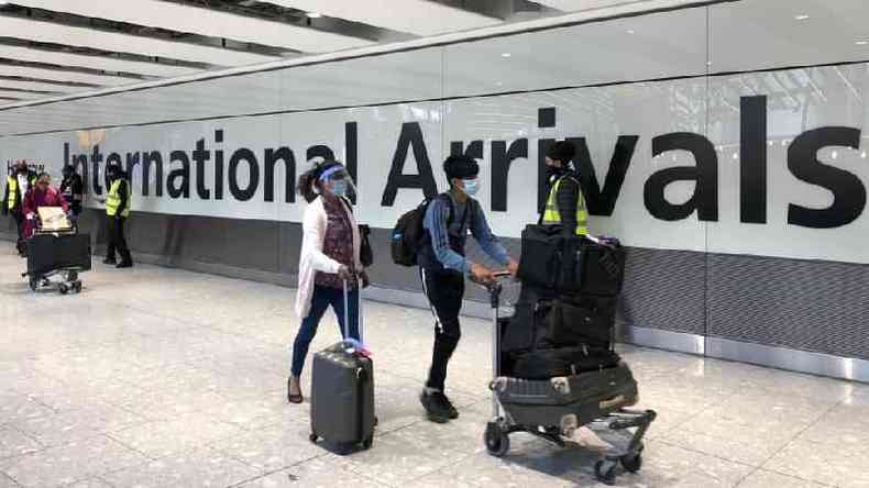 Pessoas com máscaras carregam malas em corredor de aeroporto