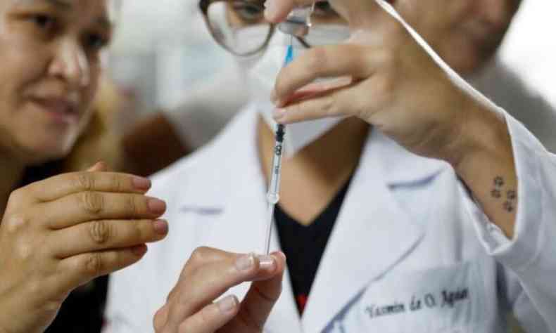 Mulher retirando vacina do vidro com agulha