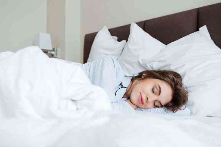 Foto de uma jovem alegre vestida de pijama est na cama em casa sob um cobertor dormindo.