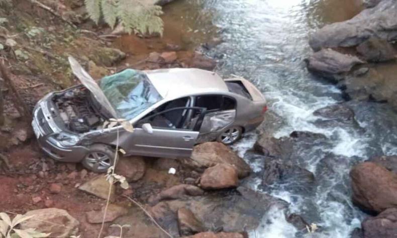 Carro prata com a parte de frente amassada e as costas em leito de rio