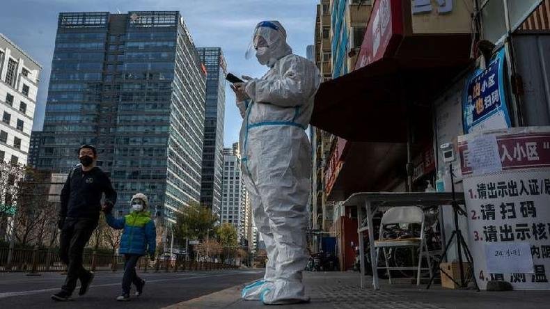 Dezenas de milhões de pessoas estão vivendo sob algum tipo de restrição na China(foto: Getty Images) Profissional de controle de covid na China em frente a um prédio, usando roupas de proteção+