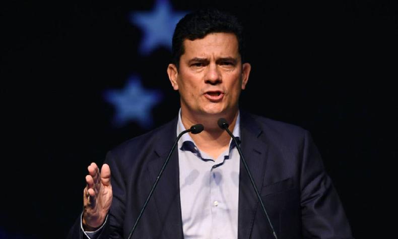 Sergio Moro falando em plpito com terno preto, camisa branca sem gravata, em um fundo preto 