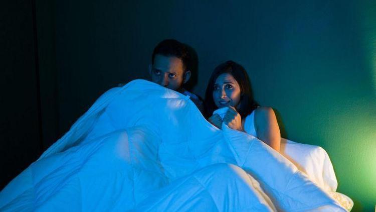 Casal olhando para televiso com expresso de medo