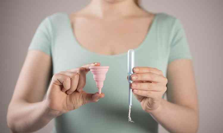 mulher segura um coletor menstrual e um tampo