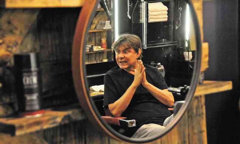 Imagem de Lô Borges, de camiseta preta, projetada em espelho de barbearia 
