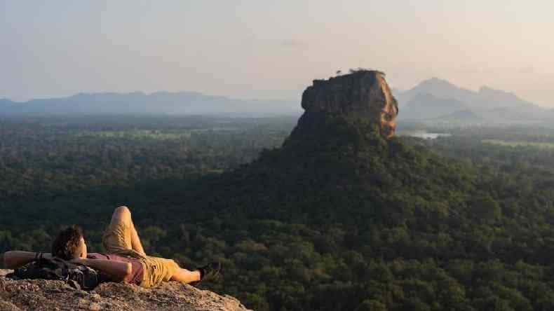 Um turista deitado, olhando para Lion Rock em um vale de rvores