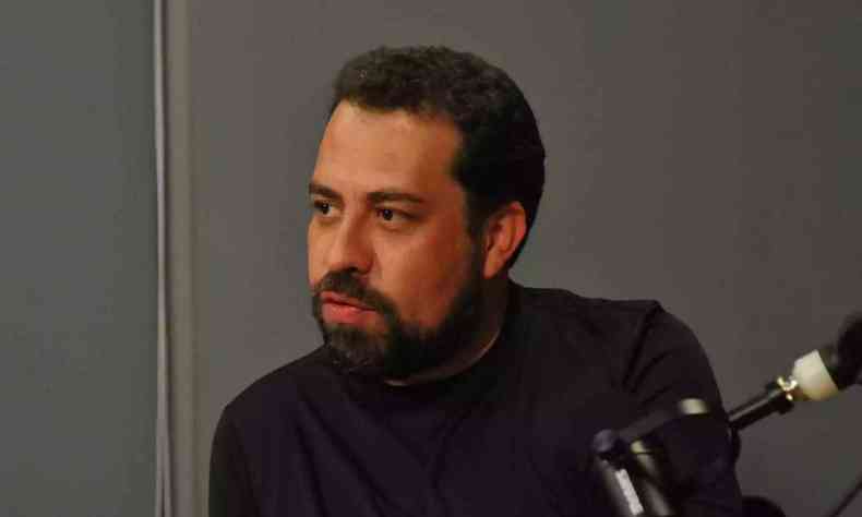 Guilherme Boulos aparece de camisa preta com fundo escuro