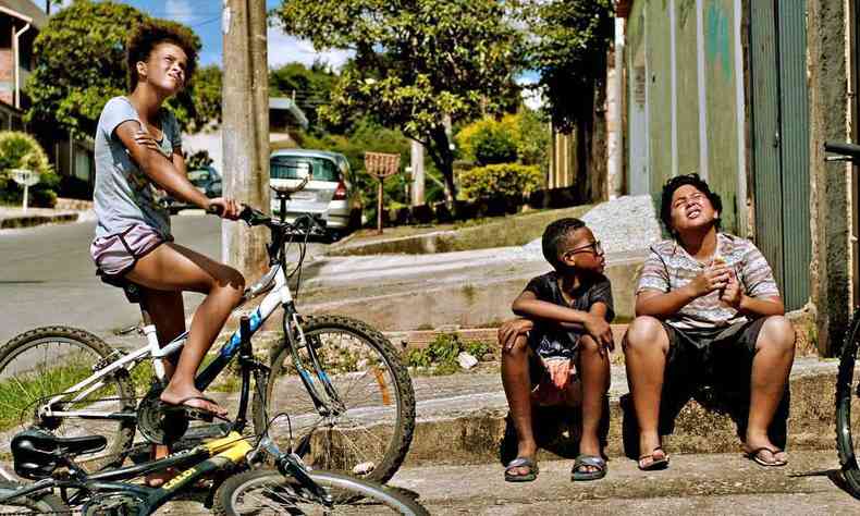Garota de bicicleta e garotos sentados no meio-fio observam o céu em cena do longa