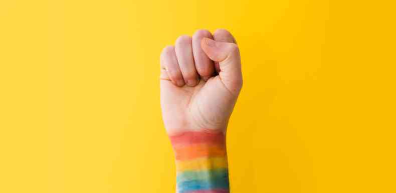 Mo direita erquida e fechada, aparecendo at o punho, pintado com as cores da bandeira LGBTQIAP+, demonstrando determinao das pessoas em lutar por espao, dignidade e respeito