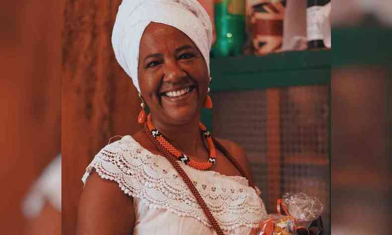 Makota Kidoial, mulher negra com roupas e turbante branco, sorrindo para a cmera