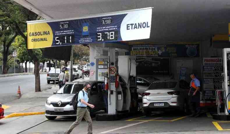 Posto de gasolina com banner com preos da gasolina e do etanol. Homem atravessa no meio.