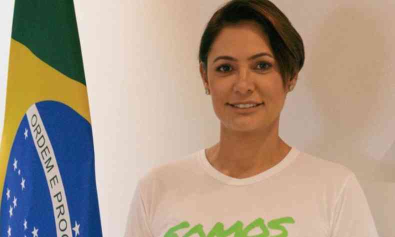 Michele  uma mulher morena, cabelos escuros curtos; ela est ao lado de uma bandeira do Brasil 