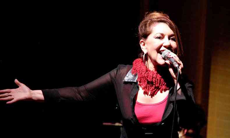 De camiseta e colar vermelhos e tnica preta, Vnia Bastos canta ao microfone em palco 