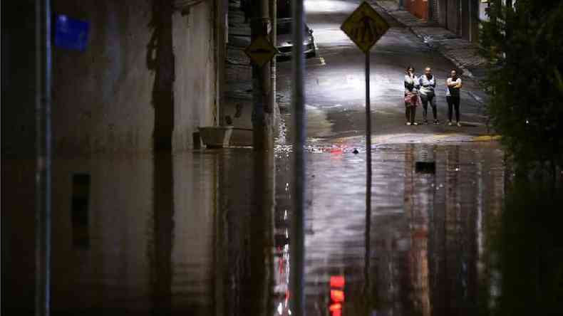Foto noturna mostra pessoas na rua observando enchente  frente delas