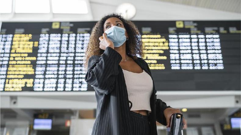 Mulher fala ao telefone em frente a painel de partidas e chegadas em aeroporto