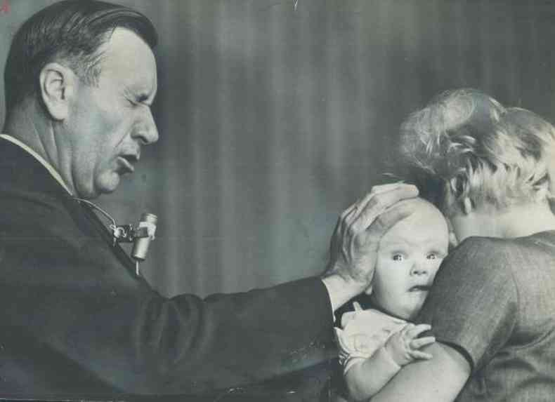 O evangelista Oral Roberts com a me sobre a cabea de um beb, que est no colo da me