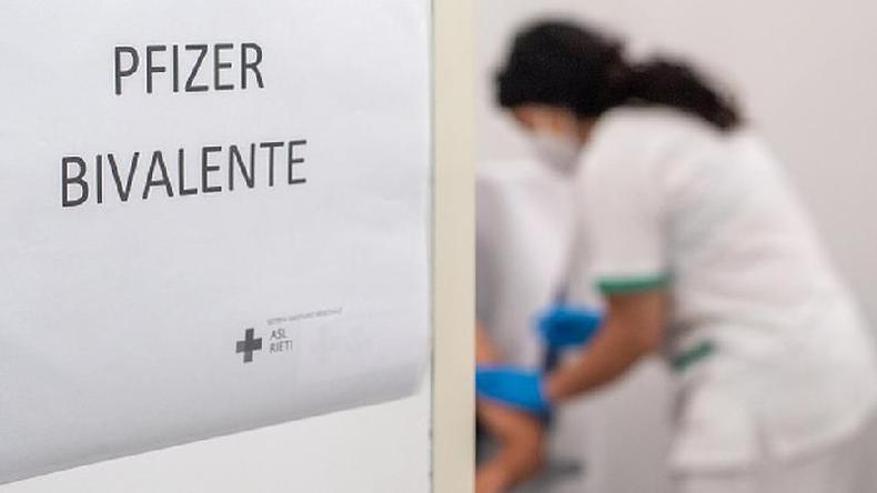 Cartas com os dizeres 'Pfizer bivalente'  ao fundo, profissional de sade aplica dose de vacina em uma pessoa