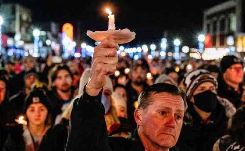 Homem segurando uma vela em frente à multidão que se reuniu em frente à escola
