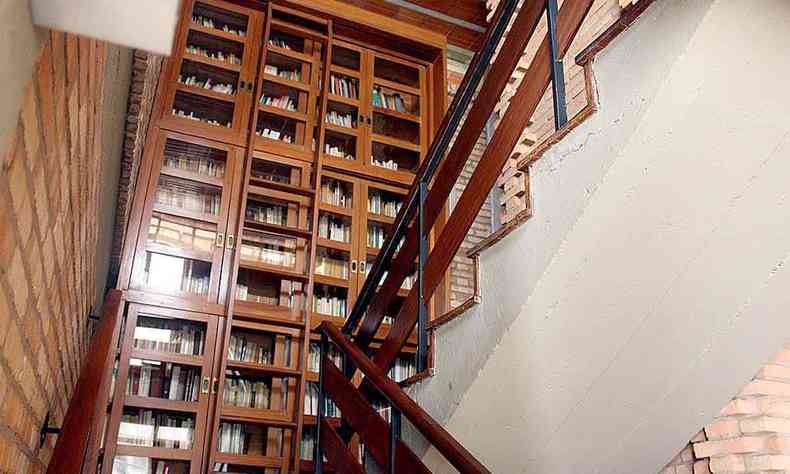 Escada tem ao fundo estante de madeira escura, cheia de livros, na casa do psicanalista Célio Garcia, em BH