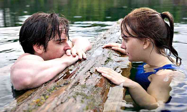 Ator e atriz mergulhados na água se olham segurando-se em tábua em cena de no ritmo do coração 