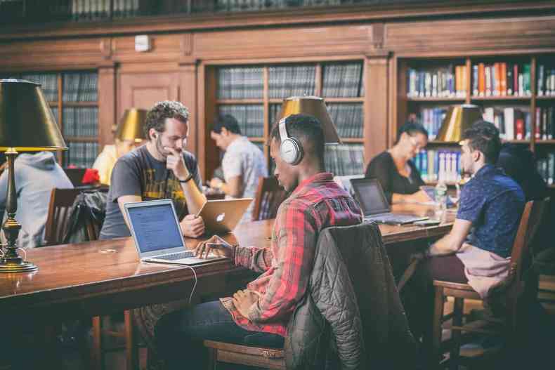 Turma de homens em uma biblioteca assistindo aula on-line