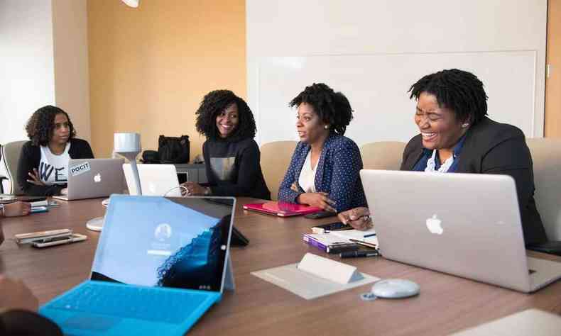 Grupo de quatro executivos negros sentados em uma mesa de reunião, com notebooks abertos