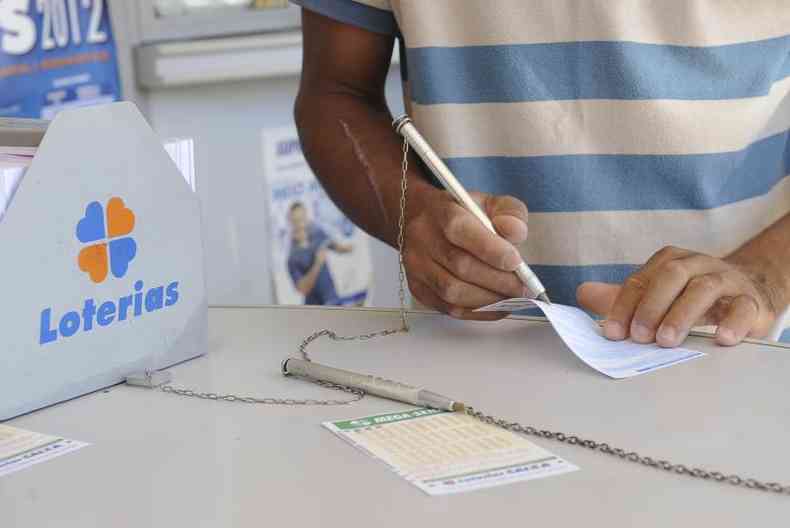 Na imagem h um homem marcando suas apostas com uma caneta no bilhete de loteria da Mega Sena 