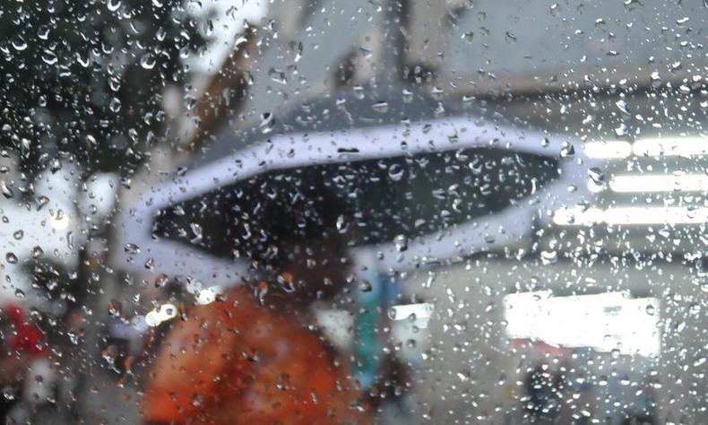 Imagem de um vidro molhado de chuva e uma pessoa de sombrinha ao fundo
