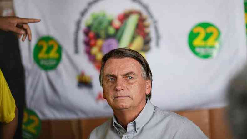 Bolsonaro olhando para o lado, em frente a pano com adesivos e seu nmero de campanha