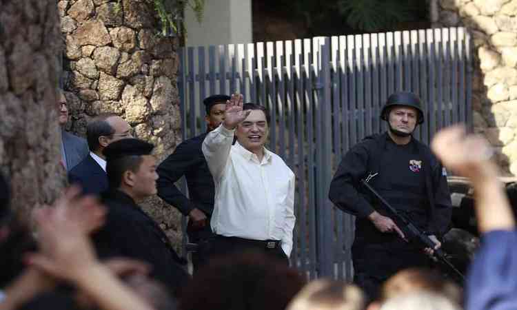 Ator que interpreta Silvio Santos em cena de O rei da TV, cercado por policiais, acena para o público