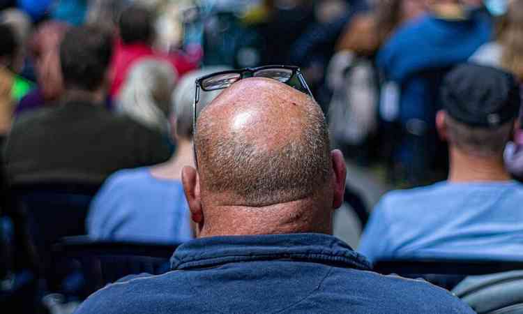 homem careca visto de costas, sentado em uma plateia