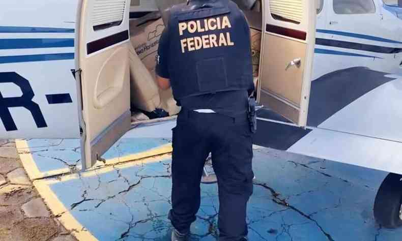 policial com uniforme da Polcia Federal apreendendo vaixas de dentro de um avio